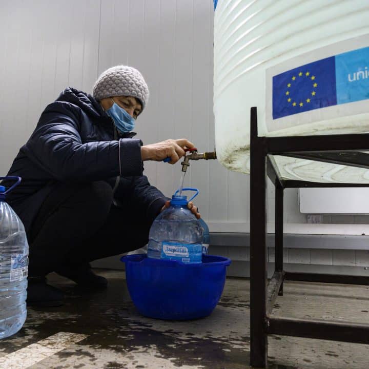 A Pishchevik, dans l'est de l'Ukraine, Larysa, 63 ans, remplit des bouteilles d'eau sur un site de distribution à un poste de contrôle local.© UNICEF/UN0432302/Volskyi