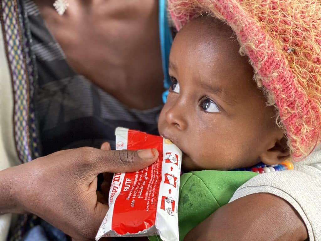 Amanuel Berhanu, tenu par sa mère, mange un peu de nourriture d'urgence après avoir subi un dépistage de la malnutrition au centre de santé Debub, dans le woreda de Wajirat, dans le sud du Tigré, en Éthiopie. UN0495650