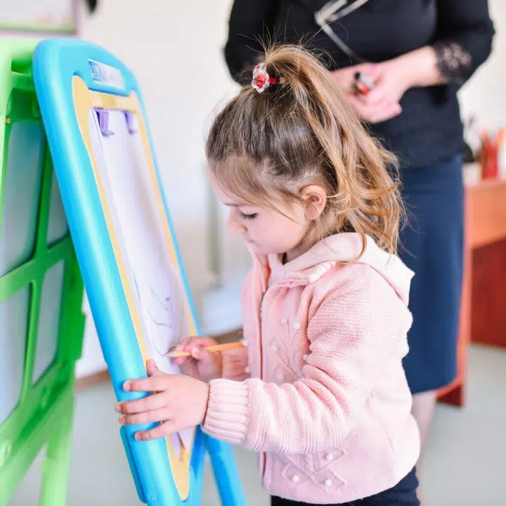 Petite fille écrivant sur un tableau blanc dans une école.