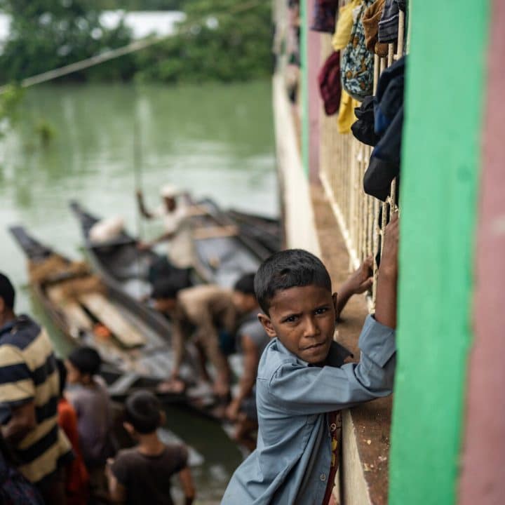 A Sylhet, au Bangladesh, un petit garçon se tient au bord d'une habitation inondée alors que des embarcations de bois sont aménagées, le 19 juin 2022. ©UNICEF/UN0657825/Mukut