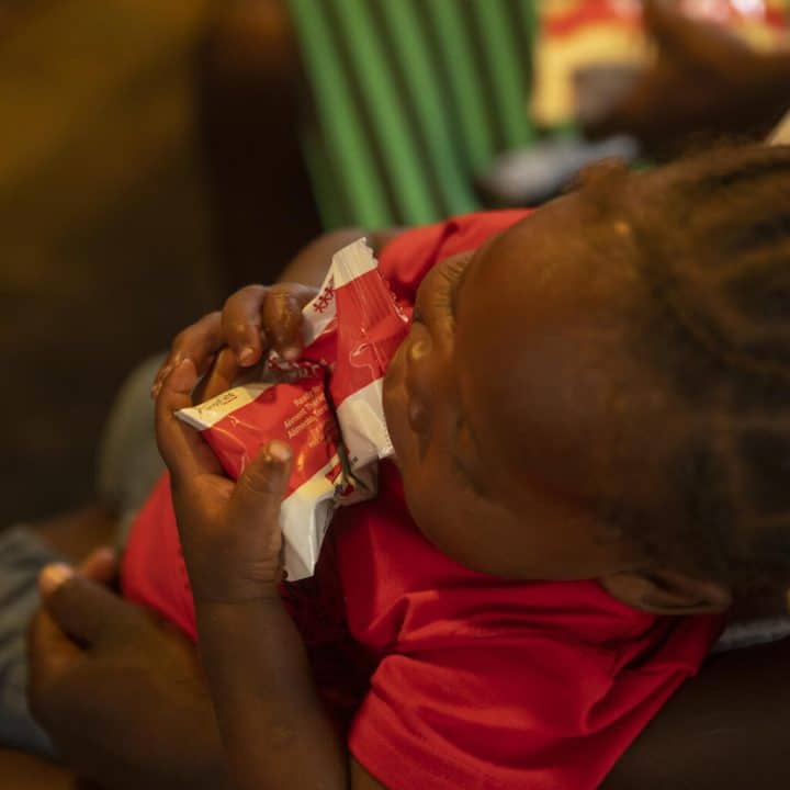 31 mai 2022, une petite fille haïtienne, assise contre sa mère, s'alimente à l'aide d'un sachet de Plumpy Nut, un aliment thérapeutique prêt à l'emploi. ©UNICEF/UN0669927/