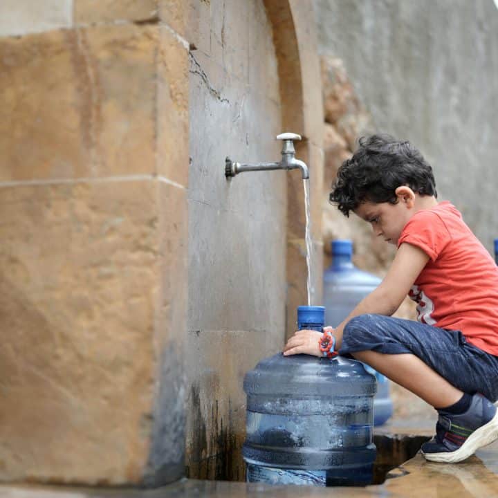 Georgio, 4 ans, aide ses parents à remplir leurs petits récipients d'eau car ils n'ont pas d'eau à la maison. © UNICEF/UN0671359/Choufany