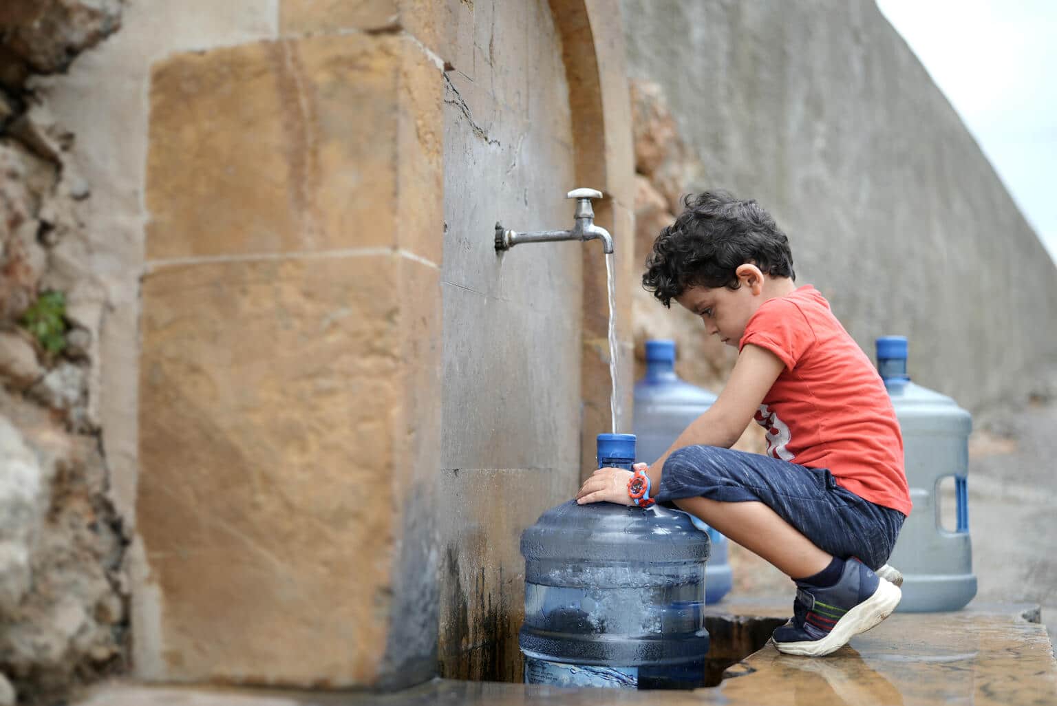 Georgio, 4 ans, aide ses parents à remplir leurs petits récipients d'eau car ils n'ont pas d'eau à la maison. © UNICEF/UN0671359/Choufany