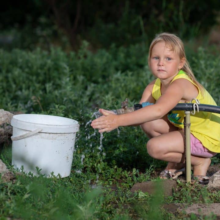 Katia, huit ans, vit à Pavlopil avec sa grande sœur, Katia, et sa grand-mère, Valentyna. Une conduite d'eau passe dans leur jardin, ce qui leur assure un bon approvisionnement. Cependant, des positions minées et militarisées se trouvent juste au-delà du champ vert derrière leur maison, faisant de la collecte de l'eau une tâche dangereuse. © UNICEF/UNI356708/Filippov