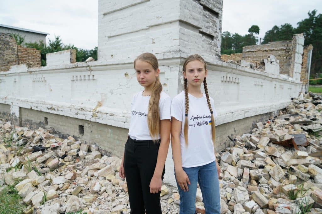 Nelya, 13 ans, et sa sœur, Lilya, 11 ans, posent devant les décombres de l’école à Kiev en Ukraine où elles auraient dû faire leur rentrée, le 20 juillet 2022. © UNICEF/UN0691233/Hrom
