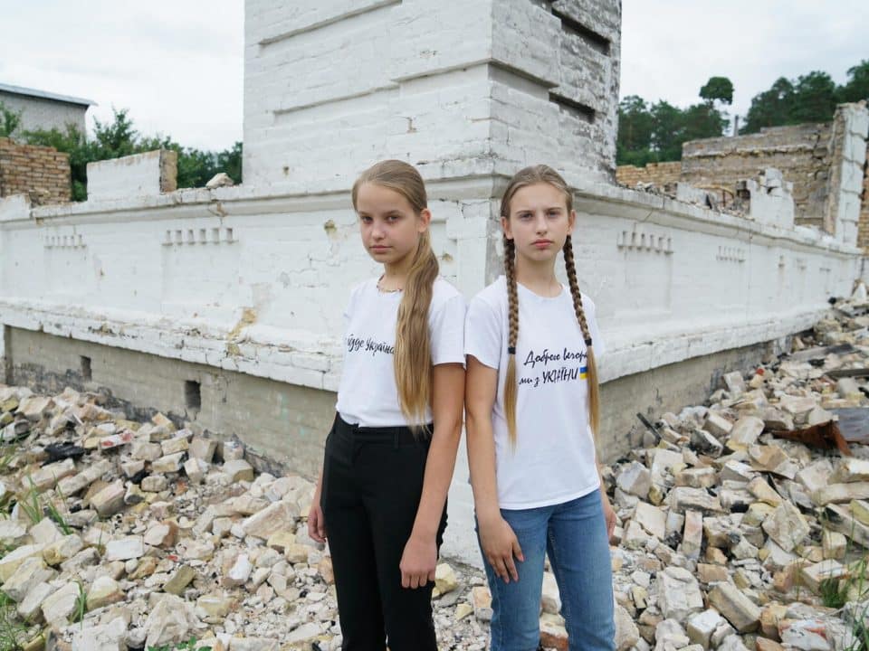 Nelya, 13 ans, et sa sœur, Lilya, 11 ans, posent devant les décombres de l’école à Kiev en Ukraine où elles auraient dû faire leur rentrée, le 20 juillet 2022. © UNICEF/UN0691233/Hrom