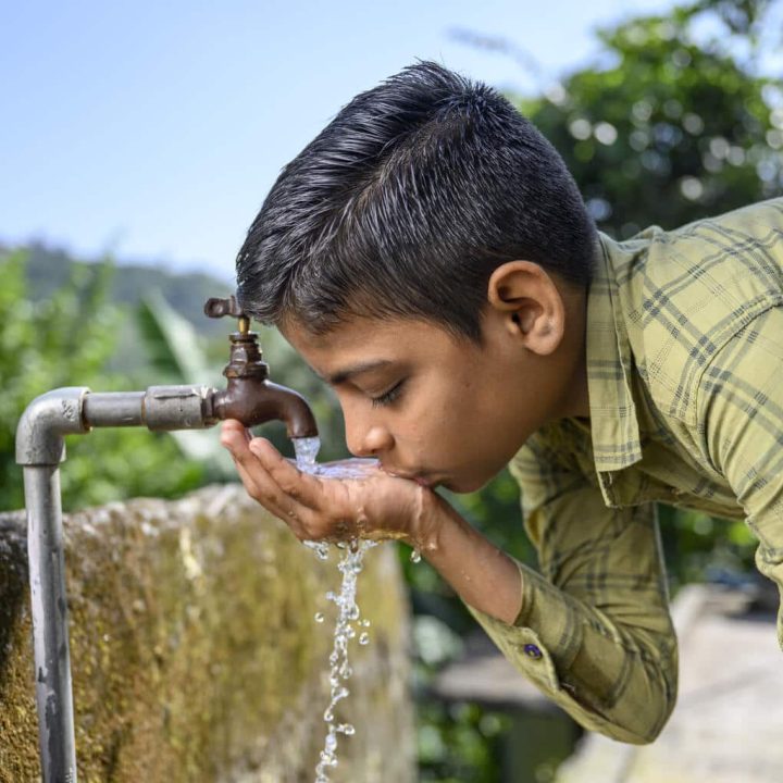 Un enfant heureux qui boit de l'eau à partir d'une source d'eau courante fournie à son village par JJM. Lieu : Village Bathol, Solan, Himachal Pradesh, Inde. © UNICEF/UN0718845/Panjwani