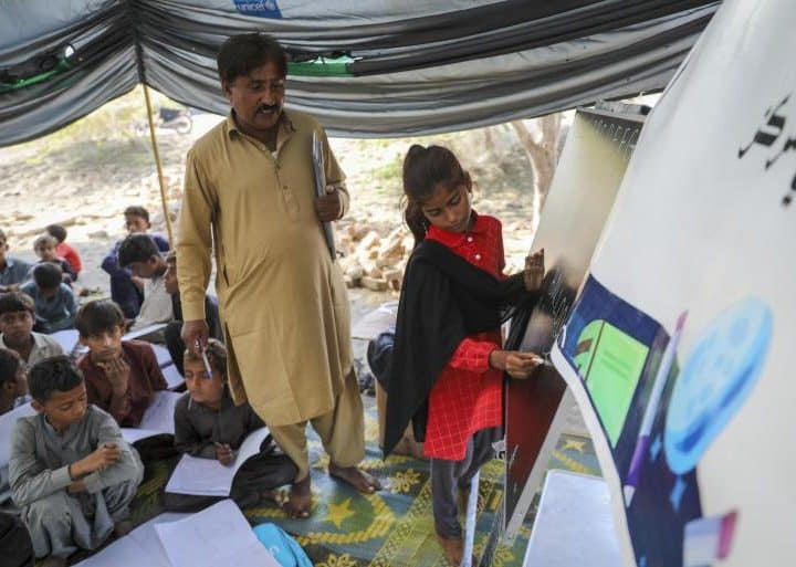Octobre 2022, Kanwal, 6 ans, écrit sur le tableau noir lors d'un cours dispensé dans un centre d'apprentissage temporaire soutenu par l'UNICEF, installé à côté de l'école primaire publique endommagée par les inondations dans le village de Kama Gul, province de Sindh, Pakistan. ©UNICEF/UN0728315/Zaidi