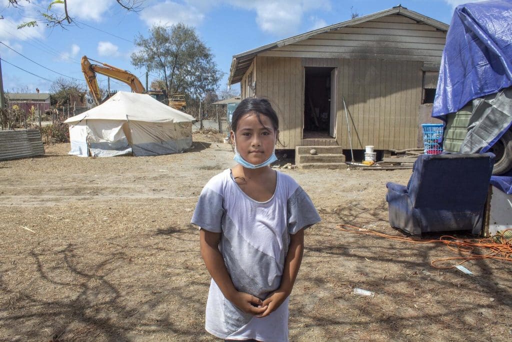 Le 22 janvier 2022, Ma'ata , 10 ans, se tient devant sa maison du village de Kanokupolu à Tongatapu, l'île principale de Tonga, montrant les dégâts causés par l'éruption du volcan sous-marin Hunga Tonga-Hunga Ha'apai et le tsunami. © UNICEF/UN0582143/Wolfgramm