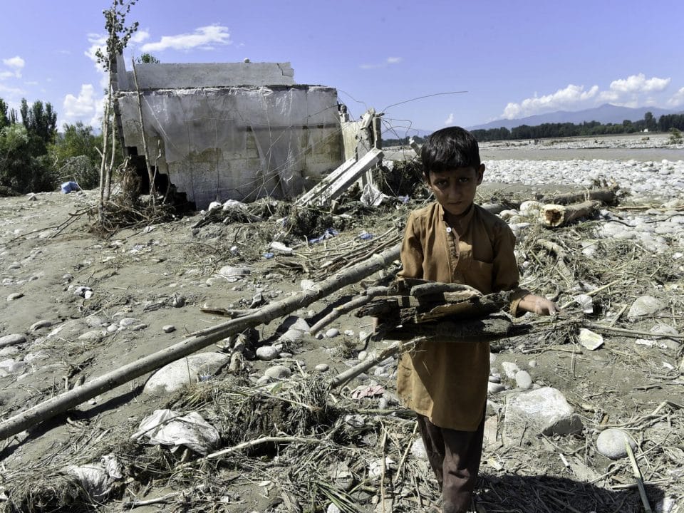 Le 28 août 2022, un garçon transporte du bois près d'une maison endommagée le long d'une rivière suite aux fortes pluies de mousson à Mingora, une ville de la vallée de Swat au nord du Pakistan, le 28 août 2022. © UNICEF/UN0698238/Majeed/AFP