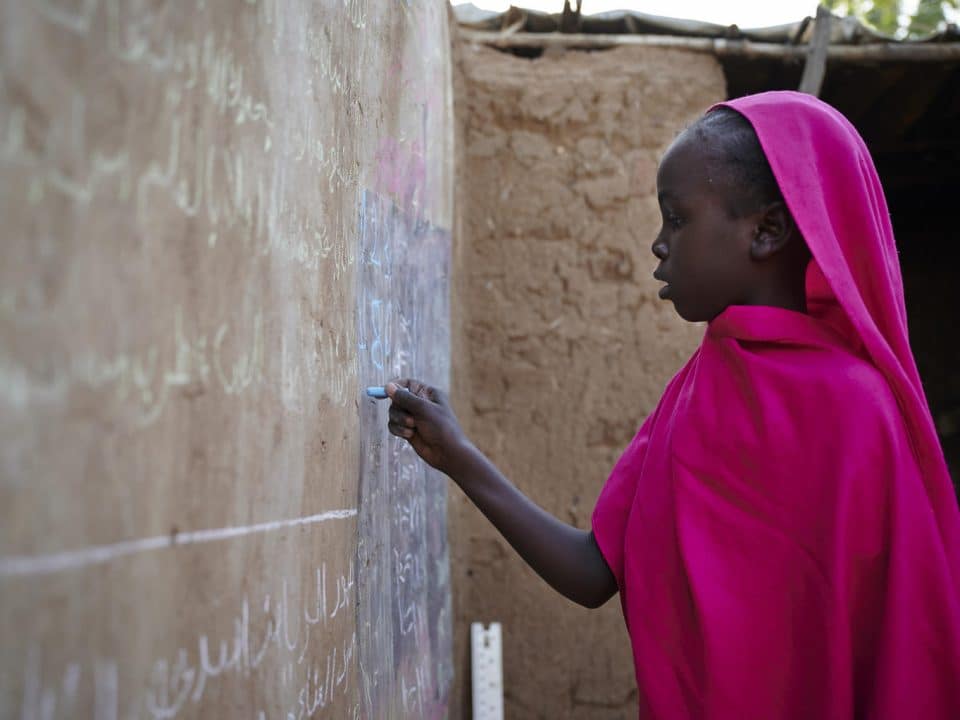 Sana, 9 ans, s'entraîne à faire ses devoirs sur un mur de sa maison dans le camp de déplacés d'Abu Shouk, non loin de la ville d'El-Fasher, la capitale de l'État du Nord-Darfour, au Soudan. © UNICEF/UNI235401/Noorani