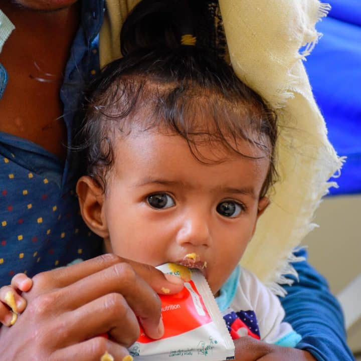 Ebtihal, 7 mois, sur les genoux de sa mère, mange un sachet de Plumpy Nut dans le centre de santé Al Aman, Gouvernorat de Hajjah, au Yémen. ©UNICEF/UN0806465