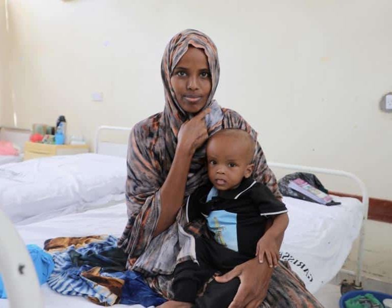 Mansuur Osman attend dans les bras de sa mère, Harira Adow, au centre de stabilisation de l'hôpital de référence du comté de Garissa. Il se remet d'une malnutrition aiguë sévère causée par la sécheresse prolongée. ©UNICEF/UN0836010/Odhiambo