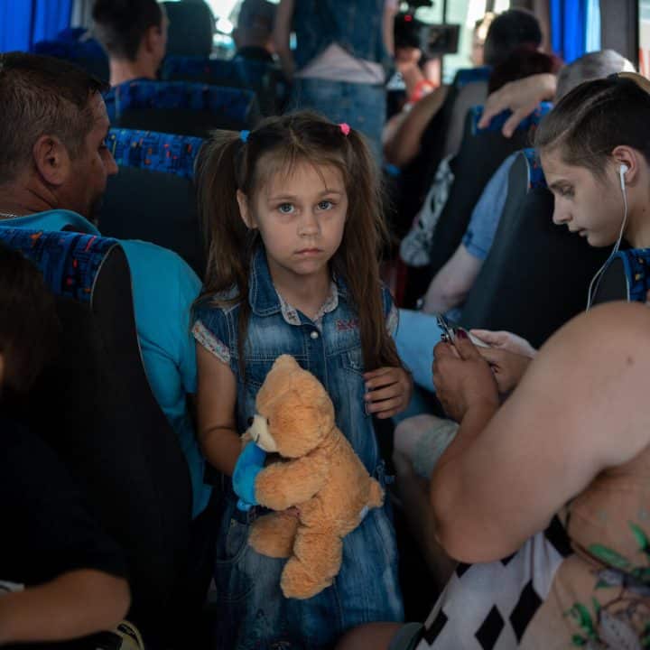 Le 7 juin 2023. Kherson, Ukraine. Dmytro, père de cinq enfants (à gauche, de dos), sa fille Anya, 7 ans, et son fils Ernest, 15 ans (à droite, avec des écouteurs) sont dans le bus d'évacuation à la gare routière de Kherson. © UNICEF/UN0853473/Filippov