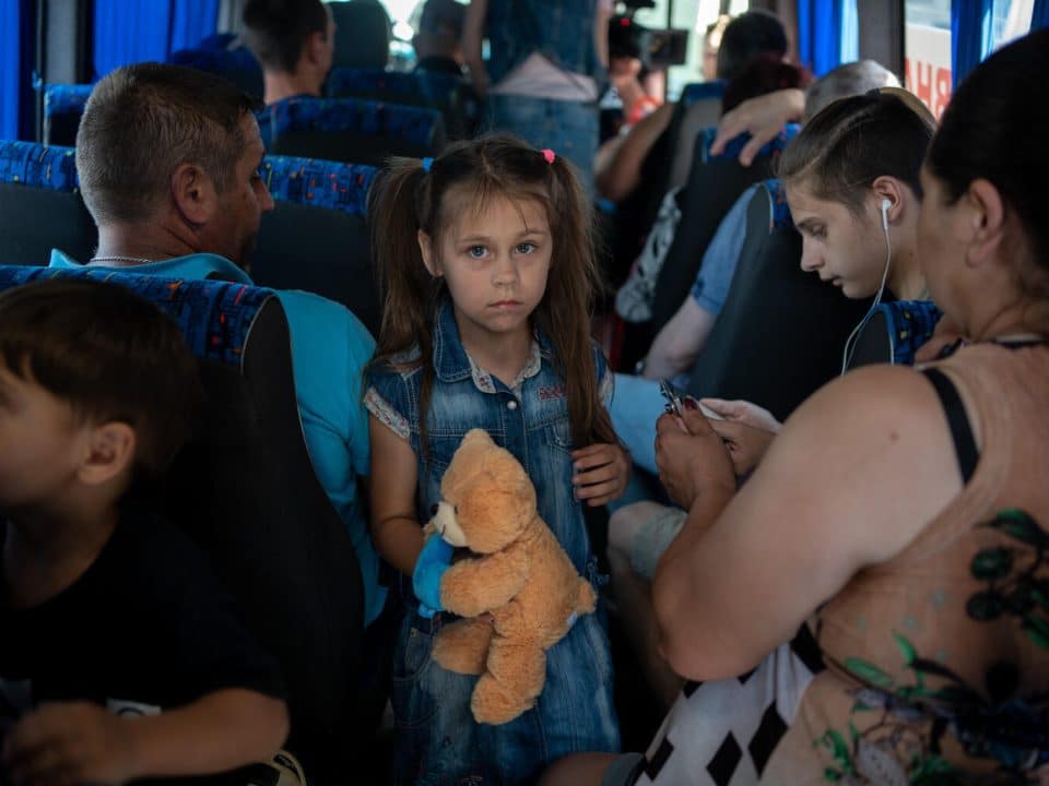 Le 7 juin 2023. Kherson, Ukraine. Dmytro, père de cinq enfants (à gauche, de dos), sa fille Anya, 7 ans, et son fils Ernest, 15 ans (à droite, avec des écouteurs) sont dans le bus d'évacuation à la gare routière de Kherson. © UNICEF/UN0853473/Filippov