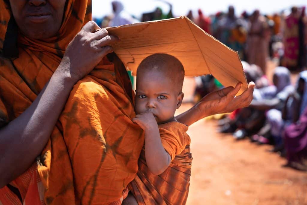 Une mère protège son fils du soleil avec un morceau de carton.