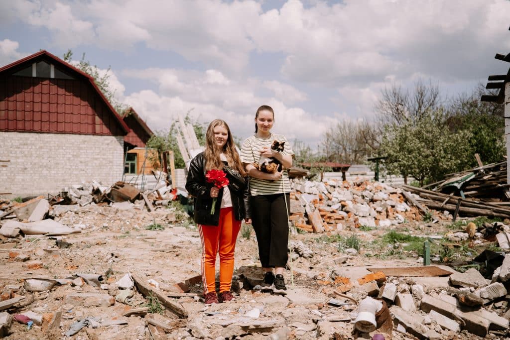 13 mai 2023, Krasnohrad, région de Kharkivska, Ukraine. Les sœurs Daiana (22 ans) et Ilona (13 ans) se tiennent dans la cour de leur maison, qui a été détruite par une roquette. Ilona tient des tulipes plantées par leur mère décédée. Daiana tient un chat. © UNICEF/UN0855525/Pashkina