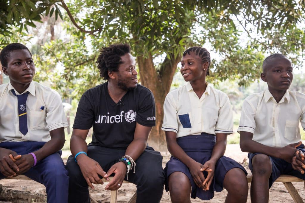 Le 22 novembre 2019, dans le village de Kabumbeh, en Sierra Leone, Ishmael Beah (en noir), auteur, ancien enfant soldat et Ambassadeur de l'UNICEF rencontre des élèves. © UNICEF/UNI229569/Tremeau