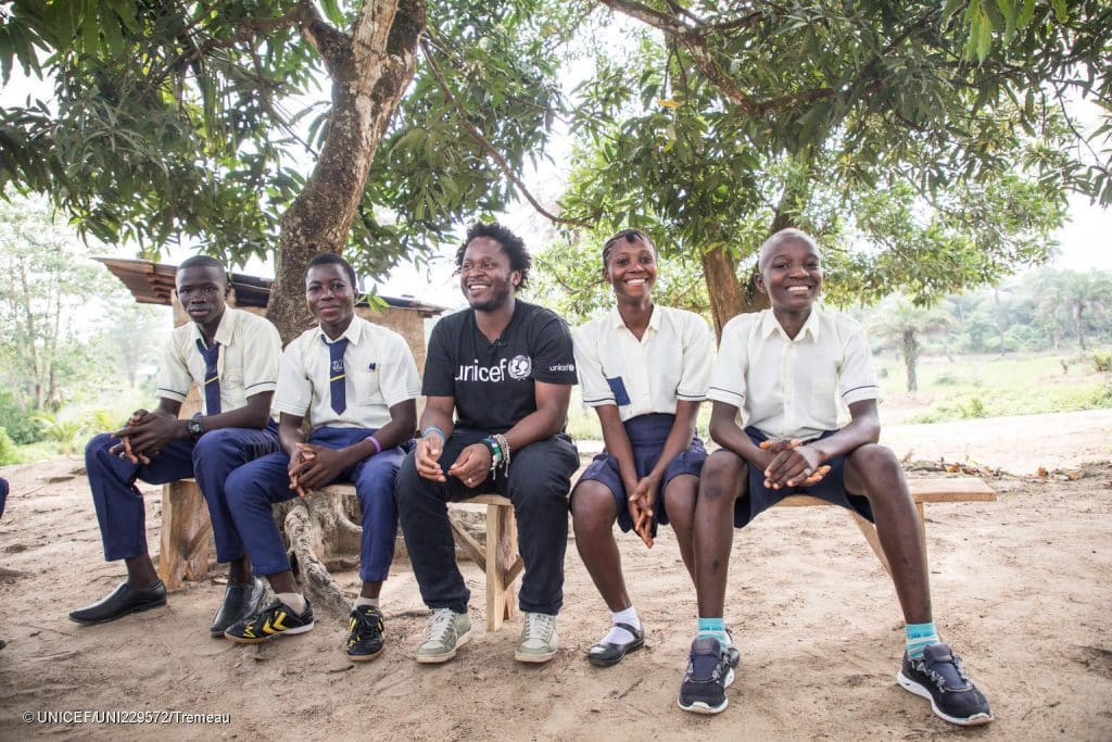 Le 22 novembre 2019, dans le village de Kabumbeh, en Sierra Leone, Ishmael Beah (en noir), auteur, ancien enfant soldat et Ambassadeur de l'UNICEF rencontre des élèves. © UNICEF/UNI229572/Tremeau