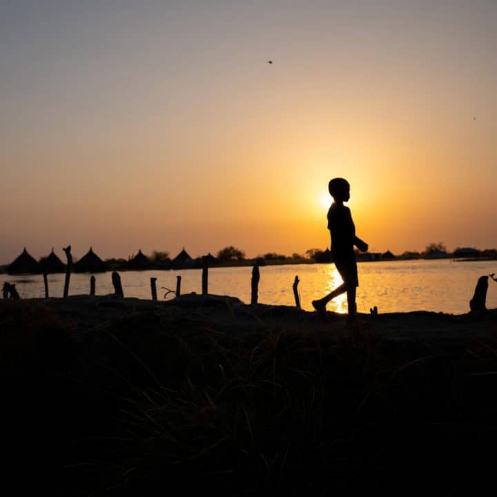 Un garçon marche le long de la digue artificielle qui sépare les eaux de crue et les maisons submergées de la zone épargnée par les inondations à Twic East, dans l'État de Jonglei, au Soudan du Sud. ©UNICEF/UN0594286/Naftalin