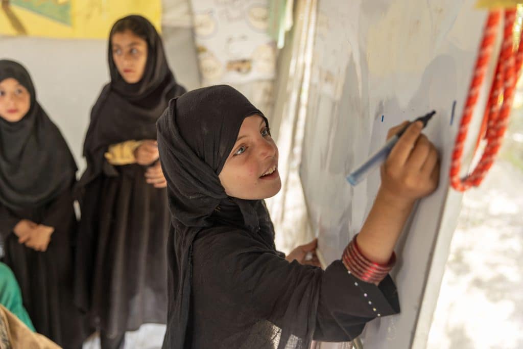 Naghma, 7 ans, écrit sur un tableau dans un espace ami des enfants où elle se rend quotidiennement avec ses amis. Cet espace adapté aux enfants a été créé dans le district de Gayan, dans la province de Paktika, en Afghanistan, un an après le tremblement de terre de juin 2022. © UNICEF/UNI399798/Bidel