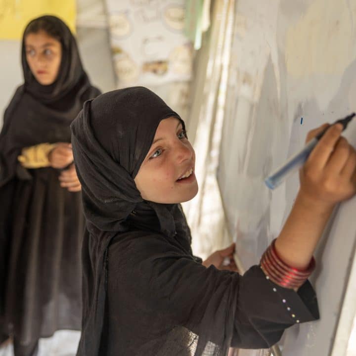 Naghma, 7 ans, écrit sur un tableau dans un espace ami des enfants où elle se rend quotidiennement avec ses amis. Cet espace adapté aux enfants a été créé dans le district de Gayan, dans la province de Paktika, en Afghanistan, un an après le tremblement de terre de juin 2022. © UNICEF/UNI399798/Bidel