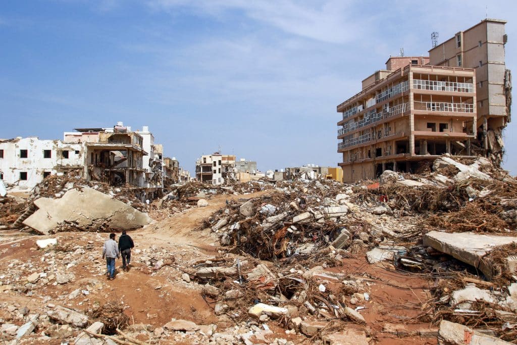 Des hommes marchent devant les débris de bâtiments causés par des crues soudaines à Derna, dans l’est de la Libye, le 11 septembre 2023. © UNICEF/UNI435002/AFP