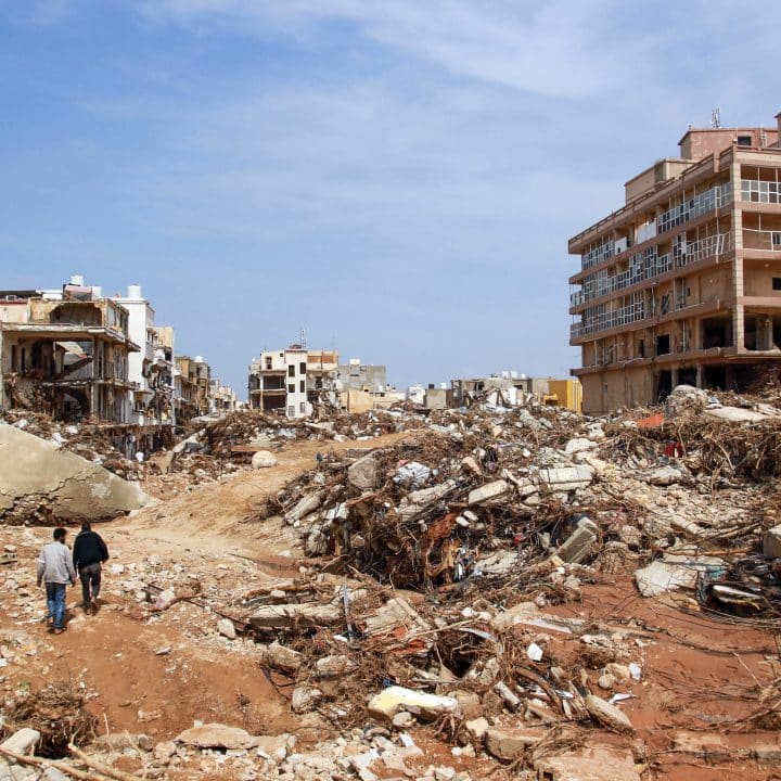 Des hommes marchent devant les débris de bâtiments causés par des crues soudaines à Derna, dans l’est de la Libye, le 11 septembre 2023. © UNICEF/UNI435002/AFP