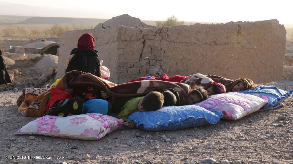 Des enfants afghans se reposent sous une couverture à côté de maisons endommagées, après le tremblement de terre dans le village de Sarbuland du district de Zendeh Jan dans la province d'Hérat le 7 octobre 2023 (Photo par Mohsen KARIMI / AFP). © UNICEF/UNI448658/Karimi AFP