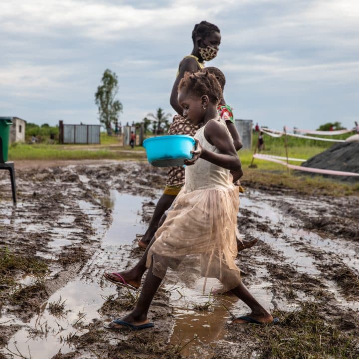 Suite au cyclone tropical Eloise, dans la province de Sofala (Mozambique), des enfants marchent dans une zone boueuse avec des conteneurs de nourriture reçus lors d'une distribution au centre de relogement de Tica, à 80 kilomètres de la ville de Beira. © UNICEF/UN0407051/Franco