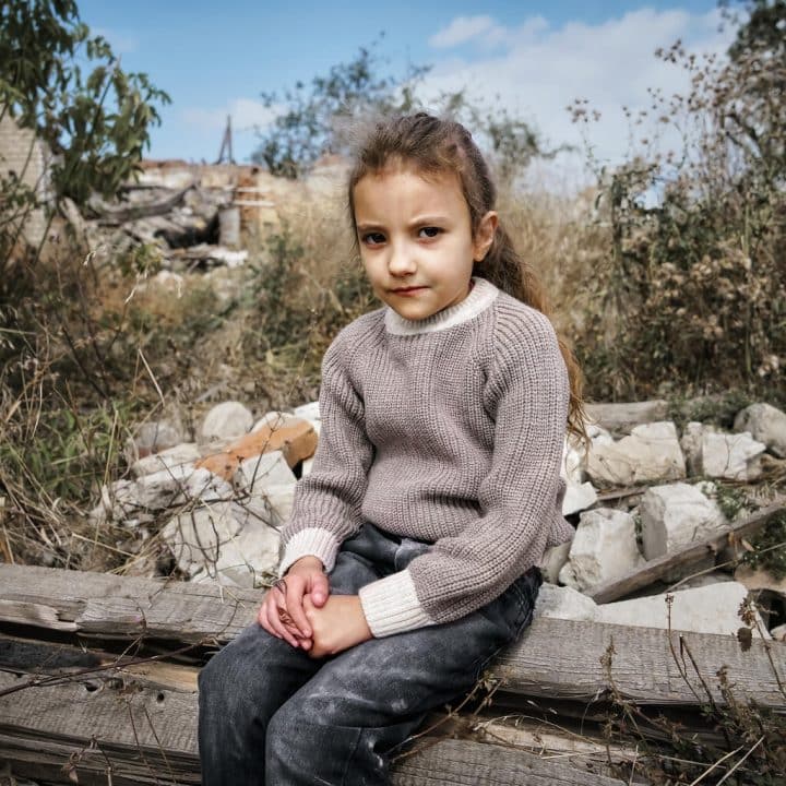 Polina a six ans. Derrière elle se trouve l'école en ruines où sa sœur aînée - Alona, 10 ans - a étudié. En février 2022, son village natal de Chistovodivka, dans le district d'Izyum de la région de Kharkiv, a été la cible de tirs. © UNICEF/UNI448418/Hrom
