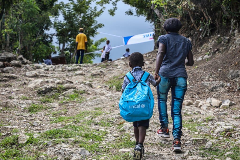 Un parent accompagne son enfant à l'école récemment reconstruite grâce à l'UNICEF dans la communauté de Jaquin, département de la Grand'Anse, en Haïti. ©UNICEF/UNI465833/Joseph