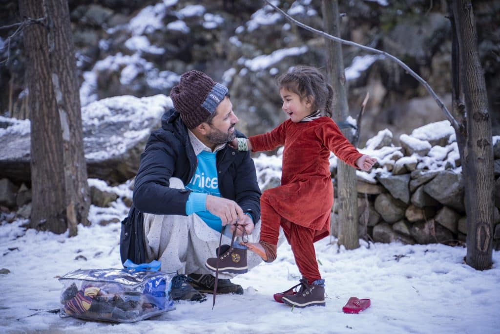 Le 1er février 2023 au Pakistan, Zaheer Ahmad, responsable de la planification, du suivi et de l'évaluation à l'UNICEF Pakistan, aide Muskan, 3 ans, à mettre les nouvelles chaussures qu'elle vient de recevoir dans le kit hiver fourni par l'UNICEF, lors d'une distribution dans le village de Sulool Daramdala, district de Upper Dir, province de Khyber Pakhtunkhwa. © UNICEF/UN0779309/Khan