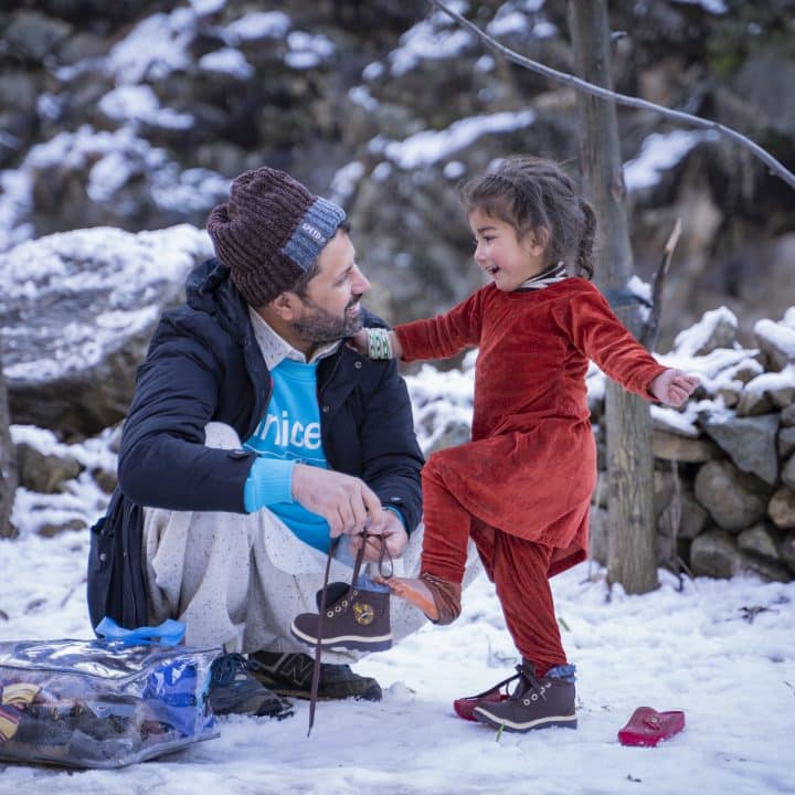 Le 1er février 2023 au Pakistan, Zaheer Ahmad, responsable de la planification, du suivi et de l'évaluation à l'UNICEF Pakistan, aide Muskan, 3 ans, à mettre les nouvelles chaussures qu'elle vient de recevoir dans le kit hiver fourni par l'UNICEF, lors d'une distribution dans le village de Sulool Daramdala, district de Upper Dir, province de Khyber Pakhtunkhwa. © UNICEF/UN0779309/Khan