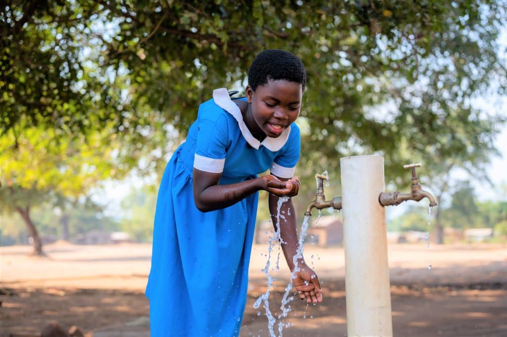 Noriah boit de l'eau à l'école grâce à un robinet installé avec l'aide de l'UNICEF au Malawi.© UNICEF/UNI427289/Khanyizira