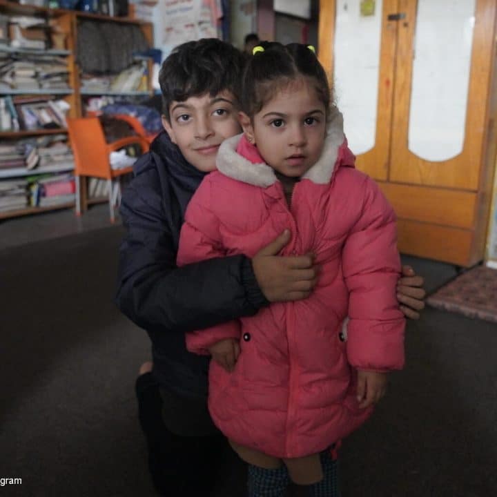 Le 13 janvier 2024, Ahmed, 10 ans, et Suha, 3 ans, posent pour une photo au Centre des femmes de Rafah, dans le sud de la bande de Gaza, actuellement utilisé comme abri, après la distribution de manteaux d'hiver, achetés par l'UNICEF et distribués par les partenaires de l'UNICEF. © UNICEF/UNI502758/Ingram