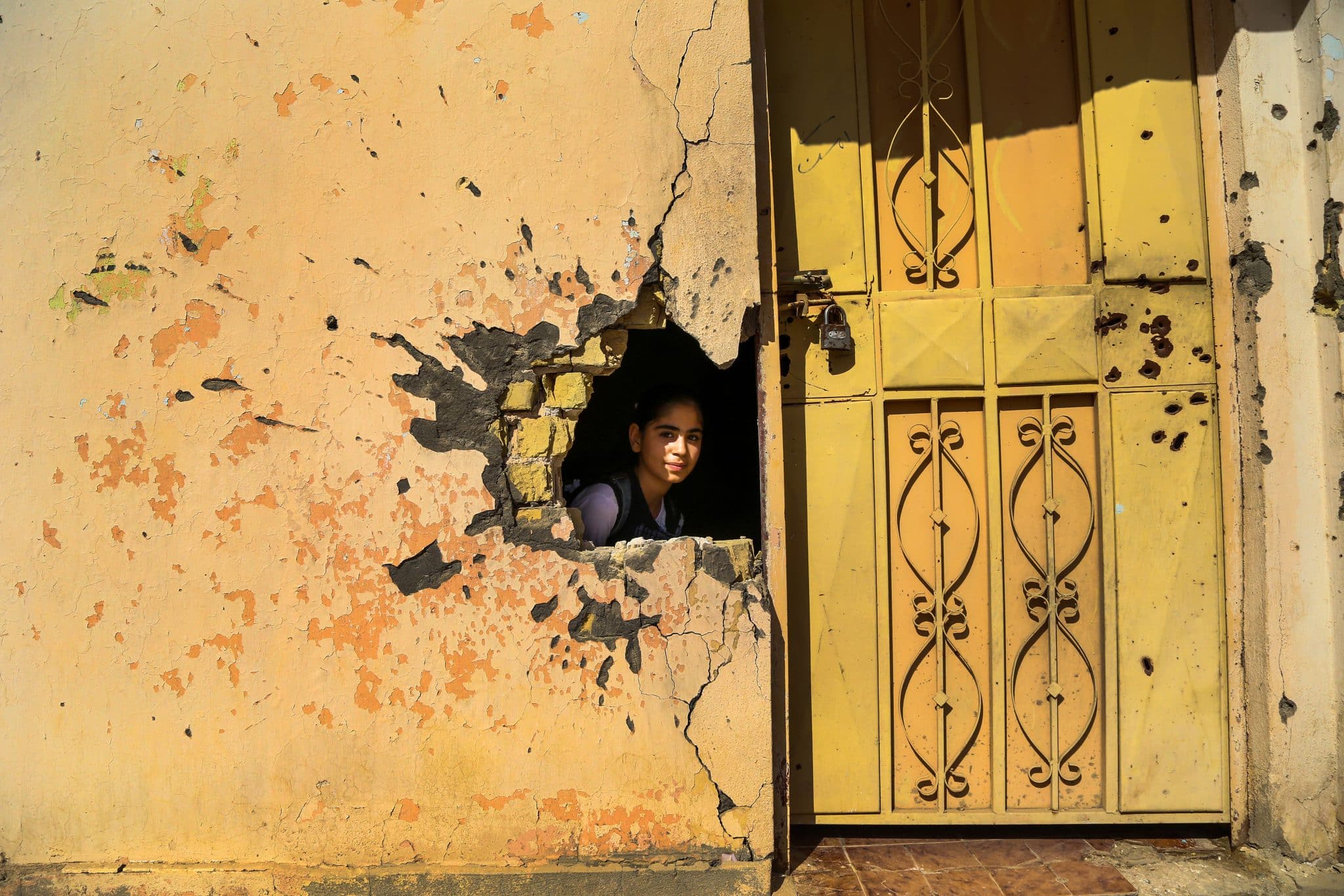 Le 1er novembre 2016, une jeune fille regarde à travers un trou dans le mur causé par les dégâts du conflit dans une école de Ramadi, dans le gouvernorat d'Anbar, en Irak. L'UNICEF travaille actuellement à la réhabilitation de 100 écoles dans l'Anbar. 3,5 millions d'enfants irakiens en âge d'être scolarisés n'ont pas accès à l'éducation, ce qui signifie qu'ils courent un risque accru de mariage précoce, de travail des enfants et d'enrôlement dans des groupes armés. Une école sur cinq n'est pas utilisée en raison du conflit. © UNICEF/UN038011/Khuzaie