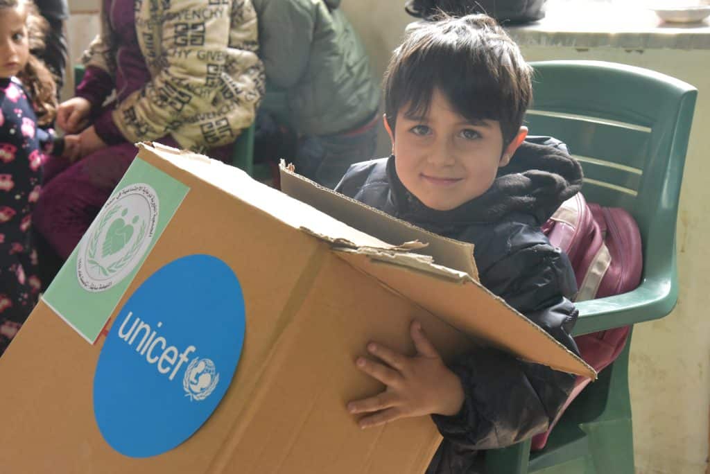 Le 8 mars 2023, Mahmoud tient le kit hiver qu'il a reçu de l'UNICEF lors d'une distribution dans une école transformée en abri collectif dans le village de Naher Al Bared, dans la région rurale de Hama, en Syrie © UNICEF/UN0825913/Hazori