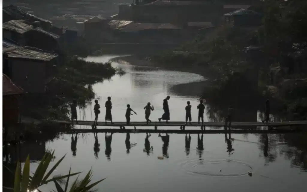 Un groupe d'enfants réfugiés rohingyas se rassemble au coucher du soleil sur un pont en bambou dans le campement de fortune de Kutupalong, jeudi 11 janvier 2018. © UNICEF/2018/Nybo