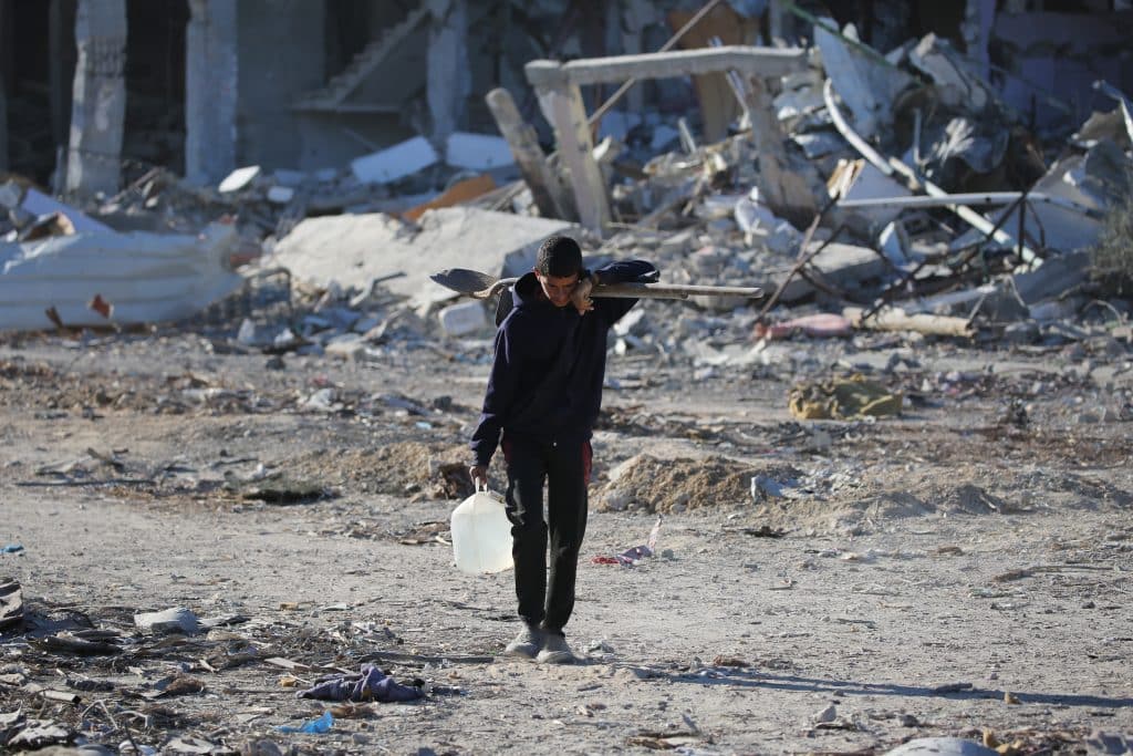 Un jeune Palestinien transporte un bidon d'eau et une pelle au milieu des ruines de maisons à Rafah, dans le sud de la bande de Gaza.© UNICEF/UNI724700/El Baba