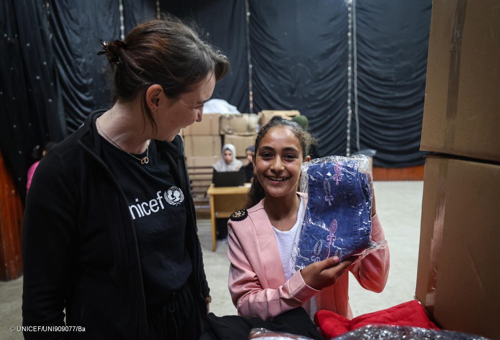 Photo prise d'une petite fille avec le staff de l'UNICEF lors d'une distribution de kits hiver dans la bande de Gaza pour soutenir les familles à affronter l'hiver. © UNICEF/UNI909077/Ba