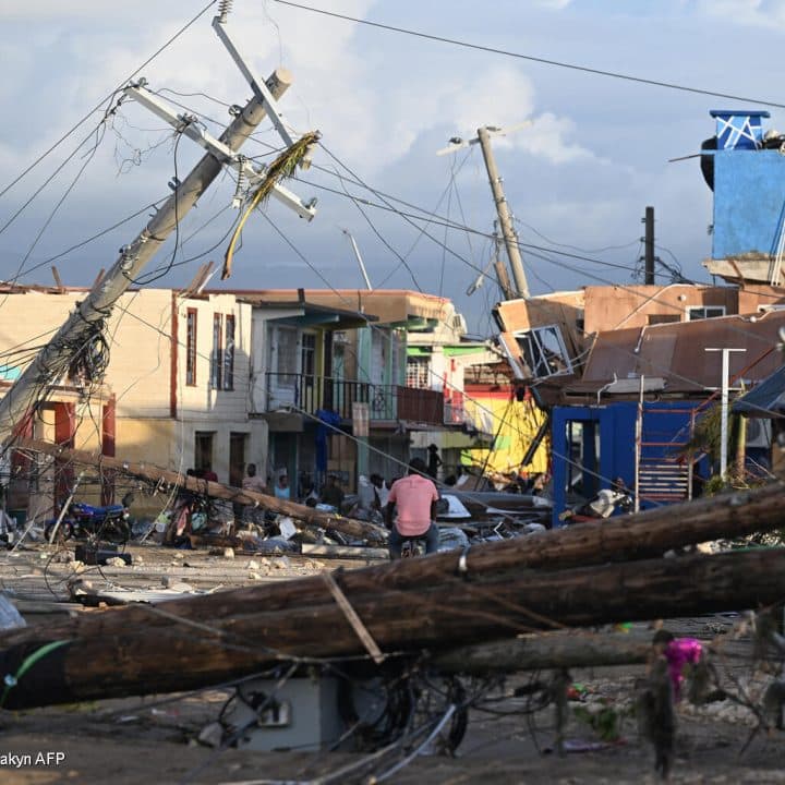 Des poteaux électriques sont tombés alors qu'un homme traverse à vélo le quartier détruit de North Street après le passage de l'ouragan Melissa, à Black River, en Jamaïque, le 29 octobre 2025. © UNICEF/UNI887331/Makyn AFP