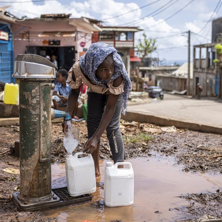 13 jours après le cyclone Chido, une fillette remplit des bidons d’eau. Les services d’accès à l’eau potable et l’électricité ne sont pas encore rétablis. Koungou, Mayotte, le 27 décembre 2024. ©Patrick Meinhardt / AF